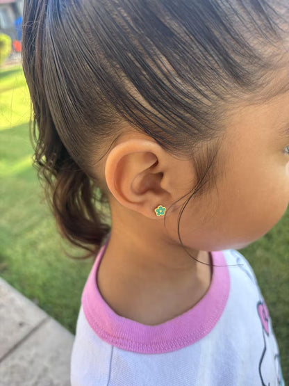 Close-up of a child's ear wearing a small green star-shaped earring with a grassy background.