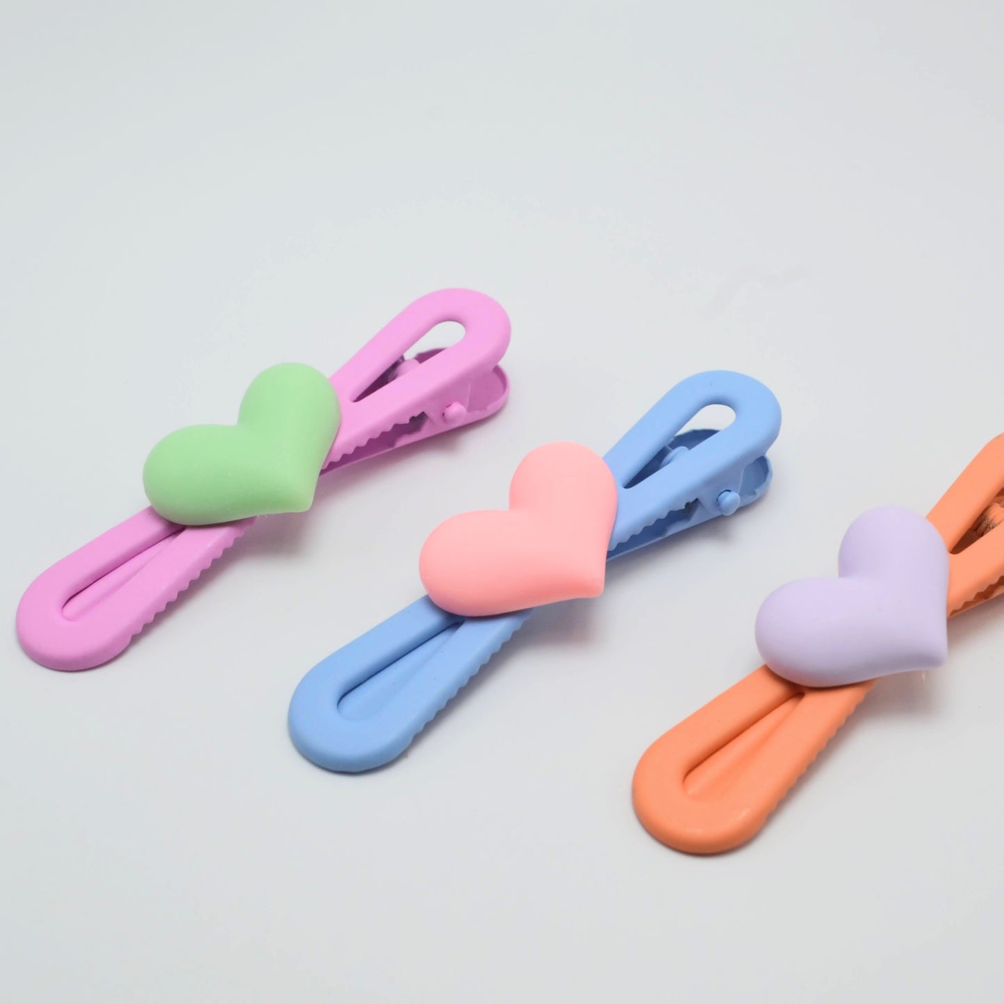 Set of four colorful heart-shaped hair clips on a light gray background