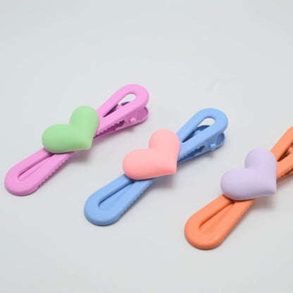 Set of four colorful heart-shaped hair clips on a light gray background