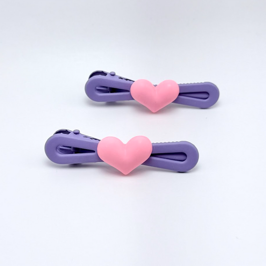 Two purple hair clips with pink heart-shaped ends on a white background