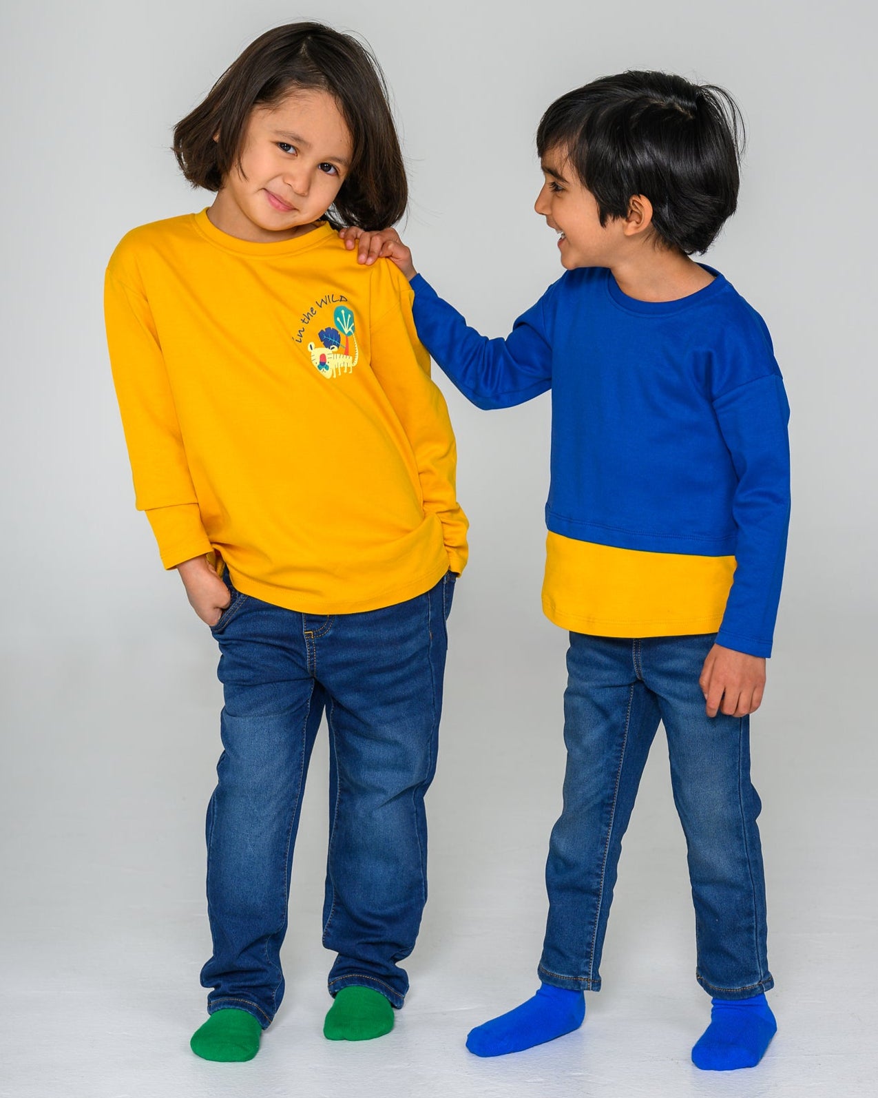 Two children wearing matching outfits with yellow and blue shirts on a white background