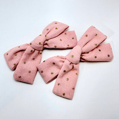 Pink knitted bow with gold embellishments on a white background