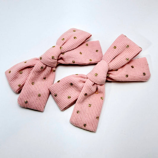 Pink knitted bow with gold embellishments on a white background