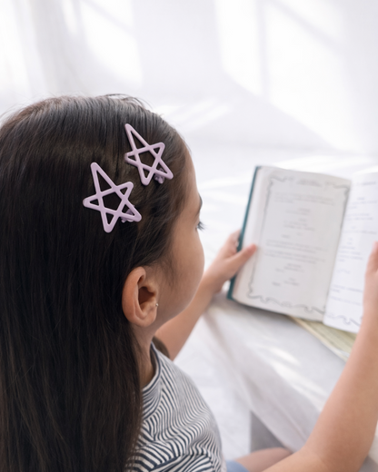 Person with star-shaped hair clips reading a book indoors.